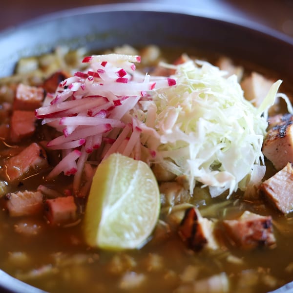 Close-up of pozole verde with chicken, hominy, shredded cabbage, radishes, and a lime wedge.