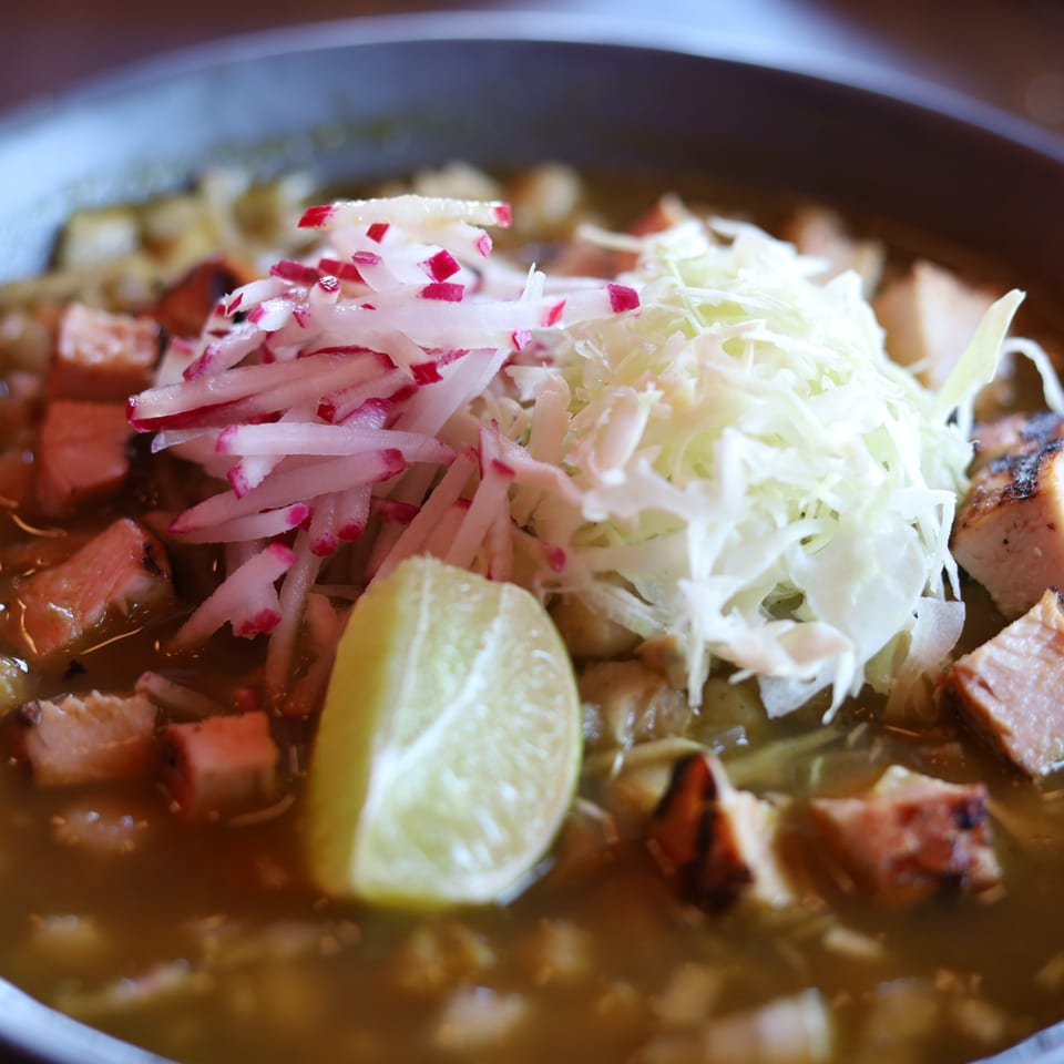Close-up of pozole verde with chicken, hominy, shredded cabbage, radishes, and a lime wedge.