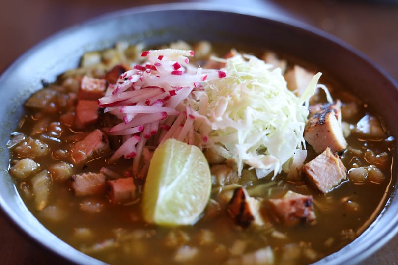 Close-up of pozole verde with chicken, hominy, shredded cabbage, radishes, and a lime wedge.