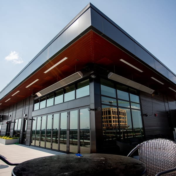 Modern rooftop restaurant patio with dark exterior, large windows, and outdoor seating under a clear sky.