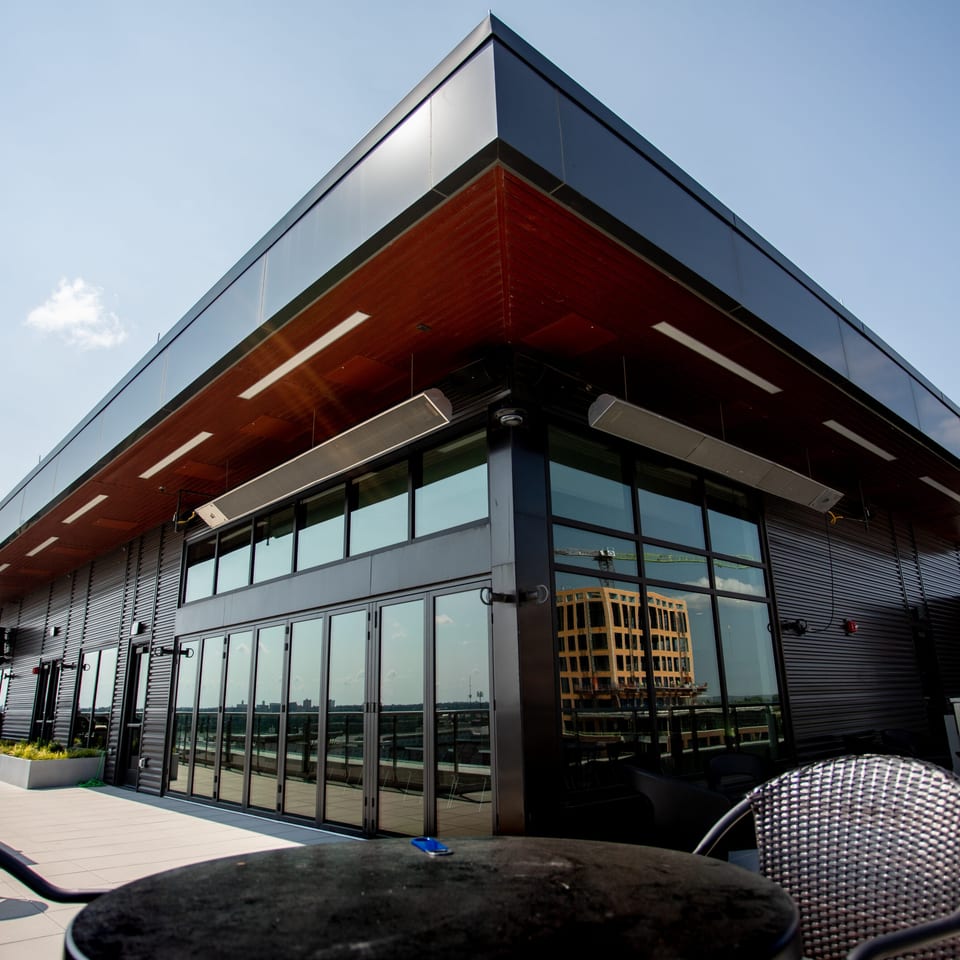 Modern rooftop restaurant patio with dark exterior, large windows, and outdoor seating under a clear sky.