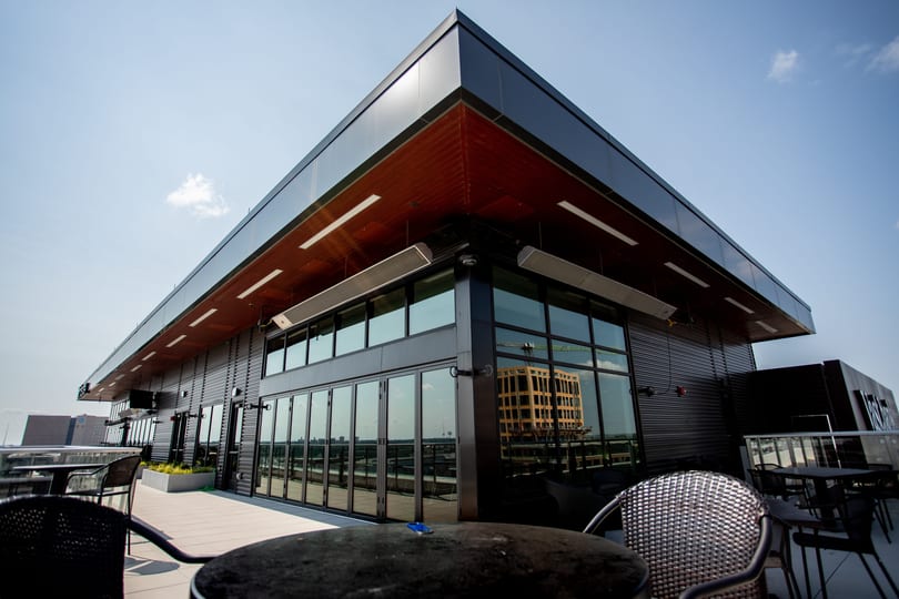 Modern rooftop restaurant patio with dark exterior, large windows, and outdoor seating under a clear sky.