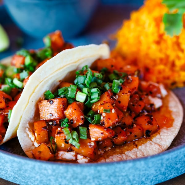 Two tacos filled with diced sweet potatoes and green onions, served with orange rice and lime.