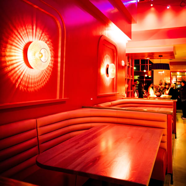 Red-lit restaurant interior with empty booths, wooden tables, and decorative wall sconces.