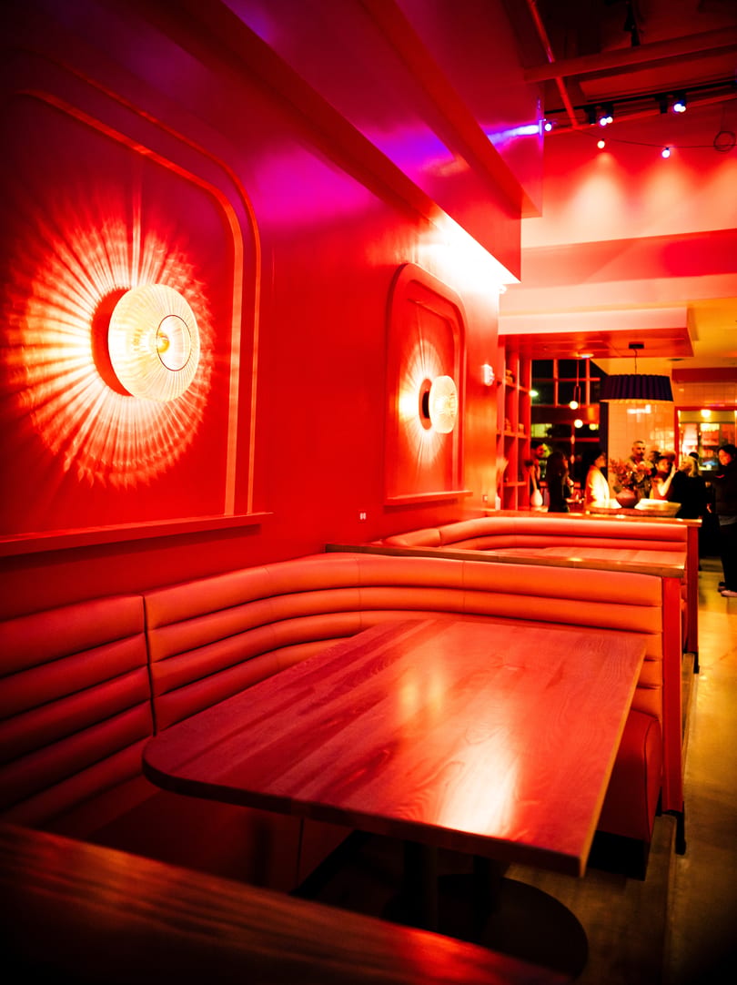 Red-lit restaurant interior with empty booths, wooden tables, and decorative wall sconces.