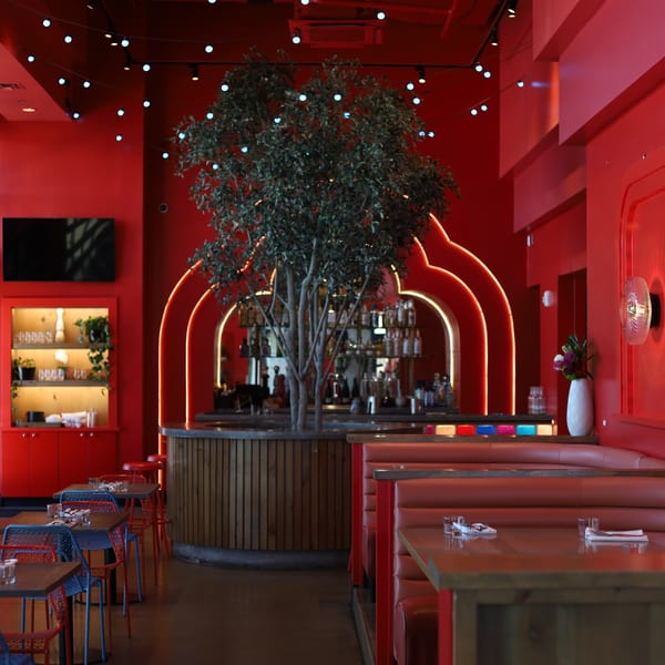 Vibrant red restaurant interior with booth seating, tables, a bar, and a large tree centerpiece.