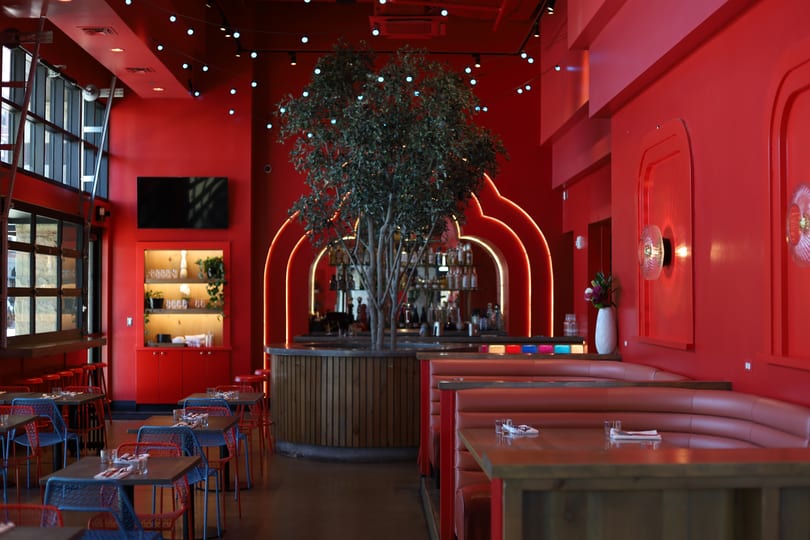 Vibrant red restaurant interior with booth seating, tables, a bar, and a large tree centerpiece.
