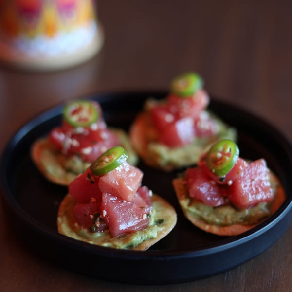 Four tuna poke appetizers with avocado and jalapeño slices on a black plate.