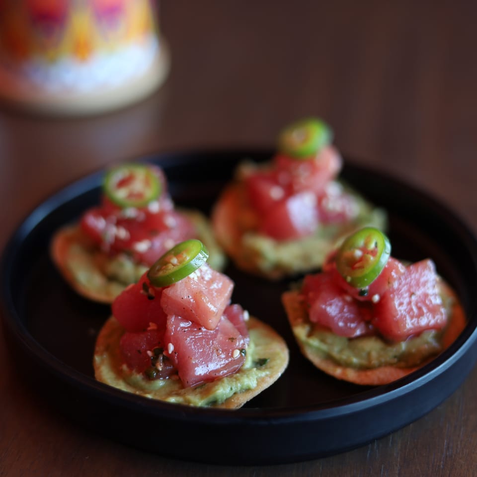 Four tuna poke appetizers with avocado and jalapeño slices on a black plate.