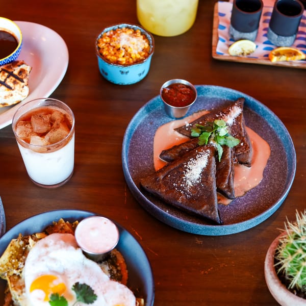 A table laden with various Mexican dishes, drinks, and a small potted cactus.