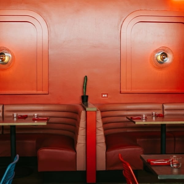 Red restaurant interior with booths, tables set with glasses and red napkins, and decorative wall sconces.