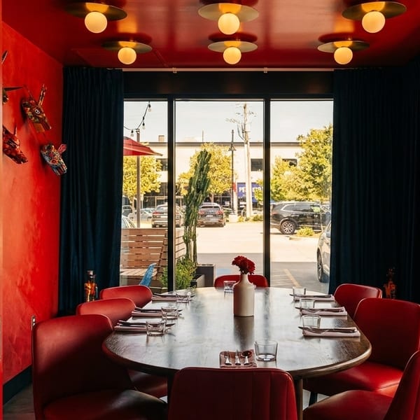 A private dining room with red walls, red chairs, a large wooden table, and a window view.